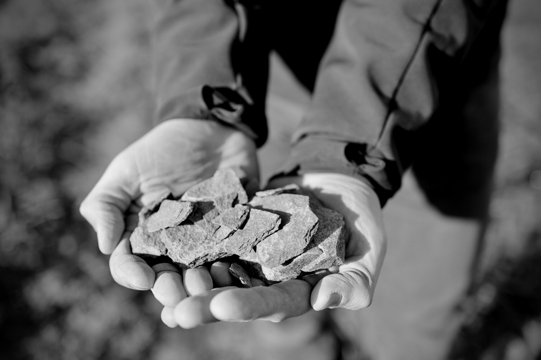 Hands holding crushed stones in black and white.